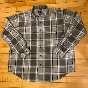 May include: A long-sleeved plaid shirt in gray and white. The shirt has a button-down collar and a button-up front.