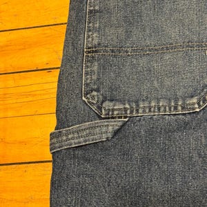 May include: Close-up of blue denim jeans, showcasing the back pocket and a utility pocket. The jeans have visible stitching and a classic design. The fabric appears worn, with a slight fade.