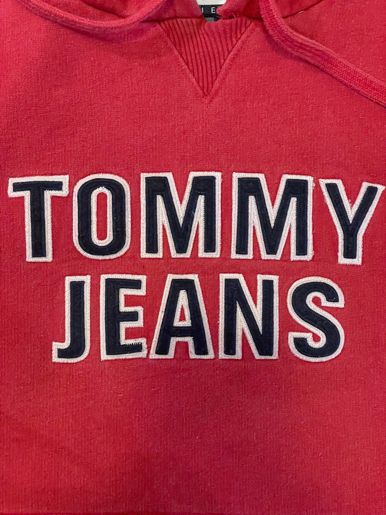 K&ouml;nnte beinhalten: Ein roter Kapuzenpullover mit dem Schriftzug "TOMMY JEANS", der in Wei&szlig; und Schwarz gestickt ist.