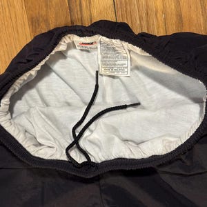 May include: Black Nike athletic shorts with a white interior lining and drawstring. The shorts have a tag with the Nike logo and text. The shorts are made of a shiny, smooth material.