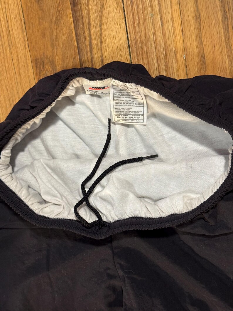 May include: Black Nike athletic shorts with a white interior lining and drawstring. The shorts have a tag with the Nike logo and text. The shorts are made of a shiny, smooth material.