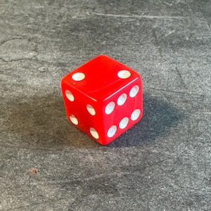 May include: A six-sided red die with rounded corners and white circular pips. The top face shows two pips, the front face shows six pips arranged in two columns of three, and the side face shows three pips arranged in a diagonal line pattern.