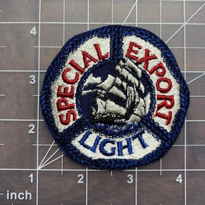 May include: A blue, white, and red embroidered patch with the words "Special Export Light" in a circle around a ship's sail.