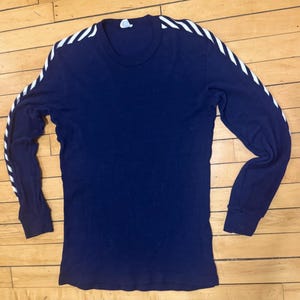May include: A navy blue long-sleeve shirt with white stripes running down the sleeves. The shirt has a crew neck and ribbed cuffs. The shirt is made of a soft, comfortable material.