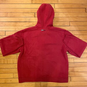 K&ouml;nnte beinhalten: Ein roter Kapuzenpullover mit einem kleinen Logo auf der R&uuml;ckseite.