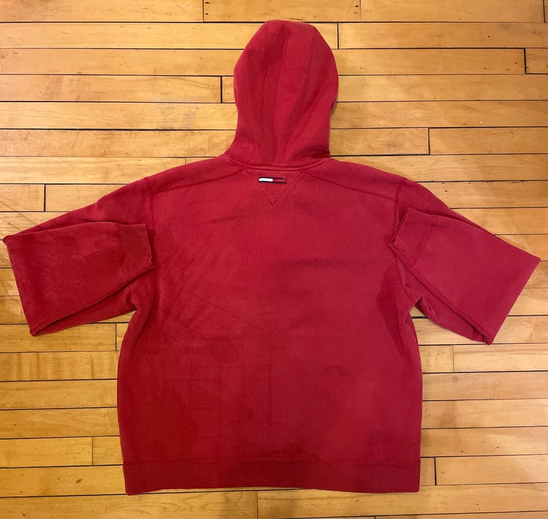 K&ouml;nnte beinhalten: Ein roter Kapuzenpullover mit einem kleinen Logo auf der R&uuml;ckseite.