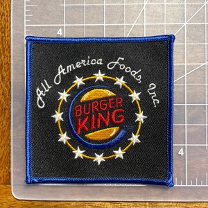 May include: A blue and black embroidered patch with the text "All America Foods Inc." and the Burger King logo in the center.