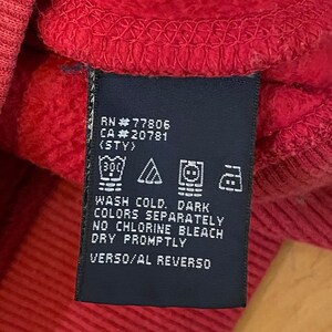 K&ouml;nnte beinhalten: Ein dunkelblaues Pflegeetikett mit wei&szlig;em Text und Symbolen. Der Text lautet "RN #77806 CA#20781 (STY) WASH COLD. DARK COLORS SEPARATELY NO CHLORINE BLEACH DRY PROMPTLY VERSO/AL REVERSO".