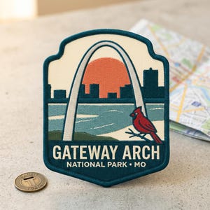 May include: A shield-shaped embroidered patch featuring the Gateway Arch in St. Louis, a large orange sun, a red cardinal bird on a branch, and a blue river. The text reads GATEWAY ARCH NATIONAL PARK MO in white capital letters on a dark blue border.