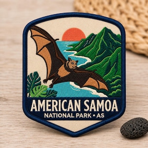May include: A shield-shaped embroidered patch featuring a flying fruit bat over a turquoise ocean, green mountains, and an orange sun. The text reads AMERICAN SAMOA NATIONAL PARK • AS in white lettering against a dark blue background border.