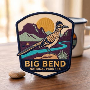 May include: A shield-shaped embroidered patch featuring a roadrunner standing on a rock in a desert landscape with mountains, a sun, and a river. The text reads BIG BEND NATIONAL PARK TX in gold lettering against a dark blue background border.