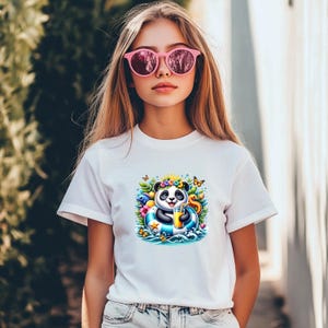 Könnte beinhalten: Ein weißes T-Shirt mit kurzen Ärmeln und einem farbenfrohen Grafikdruck eines Pandas mit Blumenkranz, der in einem blau-weiß gestreiften Schwimmring treibt und ein gelbes Getränk hält, umgeben von tropischen Blättern, Blumen und Schmetterlingen.