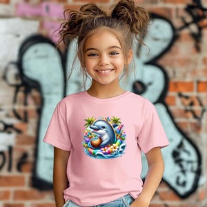 Könnte beinhalten: Ein hellrosa T-Shirt mit kurzen Ärmeln und einem farbenfrohen Grafikdruck eines grauen Delfins, der in einem regenbogenfarbenen Schwimmring treibt, ein Kokosnussgetränk hält und von tropischen Palmen, bunten Blumen und einem kleinen blauen Schmetterling umgeben ist.