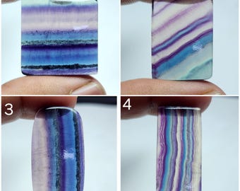 Può includere: Quattro diversi cabochon di fluorite, ognuno con un motivo unico di strisce viola, blu e bianche. I cabochon sono tutti di forma rettangolare o ovale e hanno una superficie liscia e lucida.