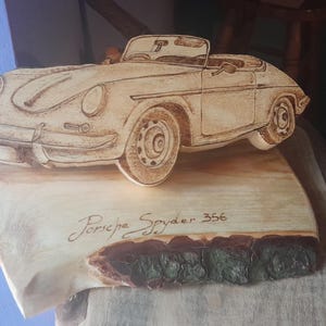May include: A wooden carving of a Porsche Spyder 356 on a wooden base. The carving is detailed and realistic, with the car's features clearly visible. The base is made of a natural wood slice, with the bark still attached.