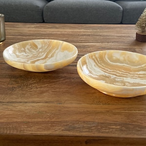 Puede incluir: Dos cuencos decorativos ovalados con un patrón arremolinado de colores crema y beige. Los cuencos están hechos de piedra pulida y se encuentran sobre una superficie de madera. Los cuencos están vacíos y son adecuados para exhibir o servir.