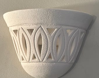 Puede incluir: Aplique de pared de cerámica blanca con un diseño de corte decorativo. La aplique tiene una forma redondeada y una superficie texturizada.