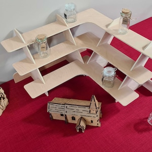 May include: A light-colored wooden corner shelf unit with three tiers, holding small glass jars with cork and metal lids. A wooden church model and a decorative wooden box are also on the red surface.