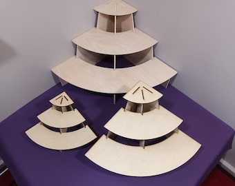 May include: Three unfinished wooden tiered display stands in varying sizes. Each stand has a triangular top and multiple curved shelves. The stands are arranged on a purple surface against a gray wall.