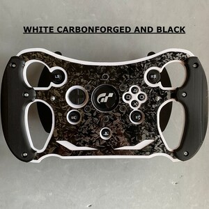 May include: A black and white racing steering wheel with a carbon fiber design. The steering wheel has a white rim and black buttons. The steering wheel has the text "WHITE CARBONFORGED AND BLACK" at the top.