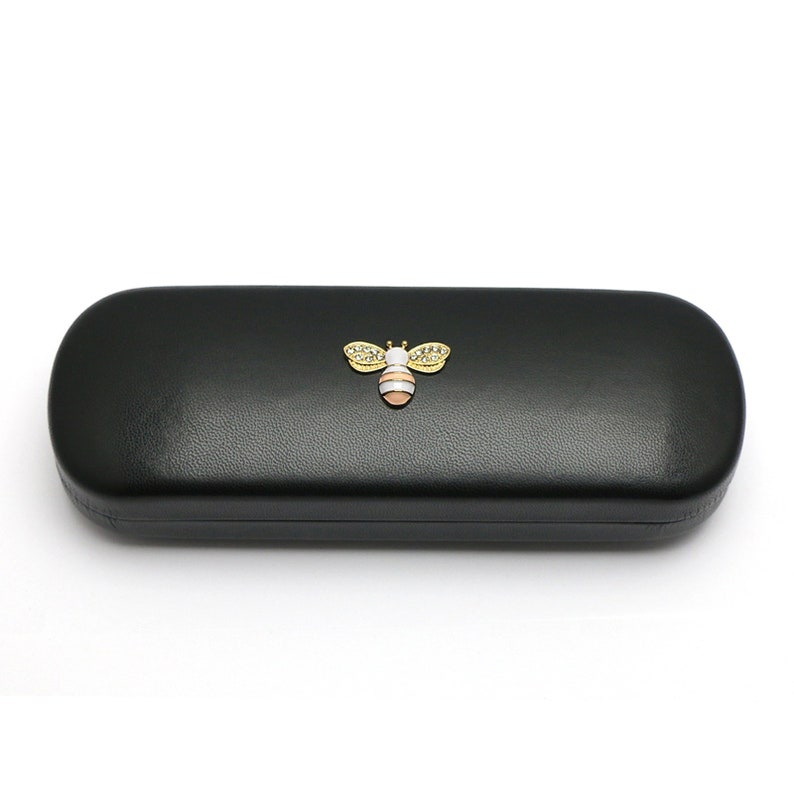 May include: Black leather eyeglasses case with a gold bee design. The bee has white wings and a pink and yellow body.