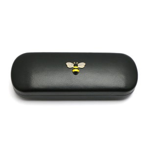 May include: Black leather glasses case with a gold bee design. The bee has yellow and black stripes and clear rhinestones.