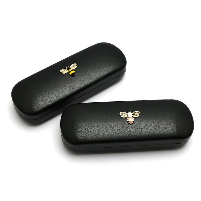 May include: Two black leather eyeglass cases with a gold bee design. The bees have yellow and black stripes and white accents.