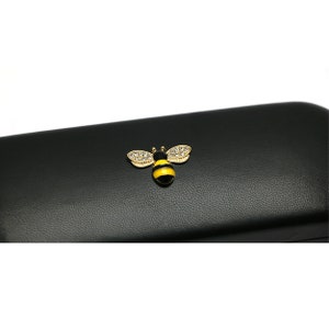 May include: Black leather glasses case with a gold bee design with yellow and black stripes and clear rhinestones.