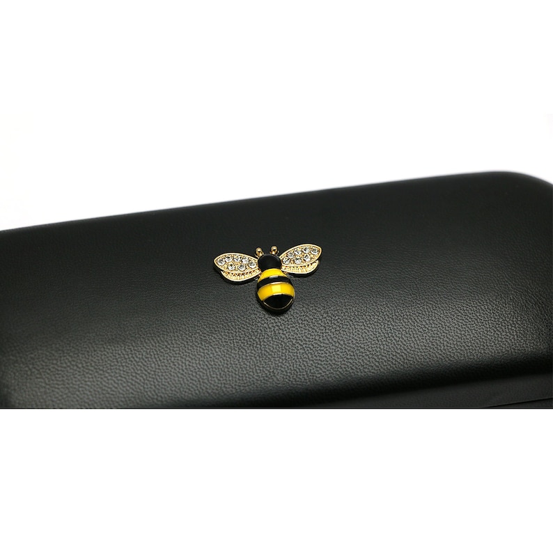 May include: Black leather glasses case with a gold bee design with yellow and black stripes and clear rhinestones.