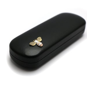 May include: Black leather glasses case with a gold and white bee design.