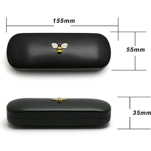 May include: Black leather glasses case with a gold bee design. The case measures 5.7 inches long, 2.2 inches wide, and 1.4 inches high.