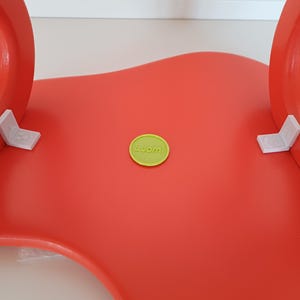 May include: A bright red, wavy, plastic chair with a green round sticker that says "Luomi" on it.