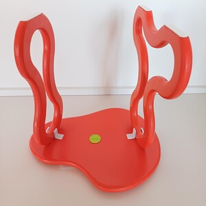 May include: A bright red, abstractly shaped stool with white accents on the legs. The stool has a smooth, glossy finish and a unique, organic design.