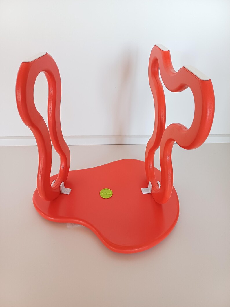 May include: A bright red, abstractly shaped stool with white accents on the legs. The stool has a smooth, glossy finish and a unique, organic design.