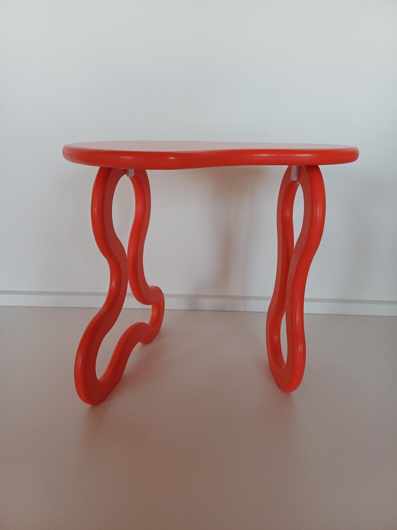 May include: A bright orange, free-form shaped side table with a rounded top and three legs. The legs are shaped like a figure eight.