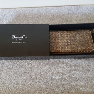 May include: A black box with the text "BrandCo Paris We Buy Luxury Bags" on the lid. The box is open and a brown woven leather wallet is inside.
