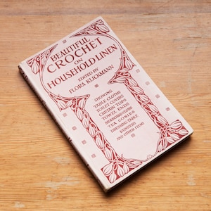 May include: A vintage book titled "Beautiful Crochet on Household Linen" edited by Flora Klickmann. The cover features a decorative floral design in shades of red and white.