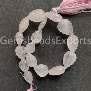 Può includere: Una collana di perline di quarzo rosa rosa chiaro, ciascuna scolpita a forma di foglia. Le perline sono infilate insieme, con un nappa rosa in alto e un piccolo filo in basso. Il testo "GemsbeadsExports" è parzialmente visibile.