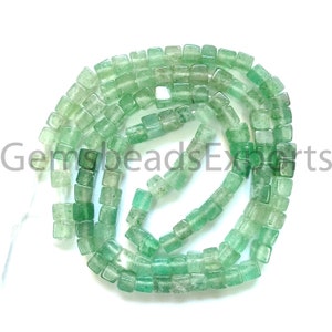 Puede incluir: Un hilo de cuentas cuadradas verde claro translúcidas. Las cuentas están ensartadas juntas, formando una forma curva sobre un fondo blanco. Las cuentas tienen una forma ligeramente irregular y un brillo sutil.