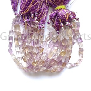May include: Strands of faceted gemstone beads in shades of lavender, peach, and clear. The beads are strung together and accented with purple and gold tassels. The gemstones have a rectangular shape and are displayed against a white background.