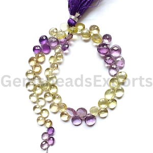 May include: A strand of faceted heart-shaped beads in alternating yellow and purple hues, arranged in a circular pattern. The beads are strung together and finished with a vibrant purple tassel at the top. The text GemsBeadsExports is visible.