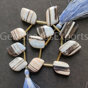 May include: A strand of polished, irregularly shaped banded agate beads featuring white, cream, and dark brown stripes. The beads are separated by thin, cylindrical gold-toned metal spacers and finished with light blue thread tassels.
