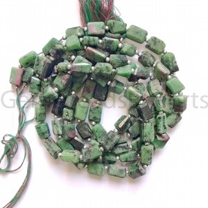 May include: A strand of green and red ruby zoisite beads. The beads are rectangular and strung together with silver-colored spacers. The string has a green and red tassel at the end. The beads have a natural, rough texture.
