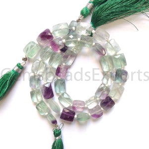 May include: A strand of faceted fluorite beads in shades of green, purple, and clear. The beads are rectangular and strung together with white string. Green tassels are attached at both ends of the strand.