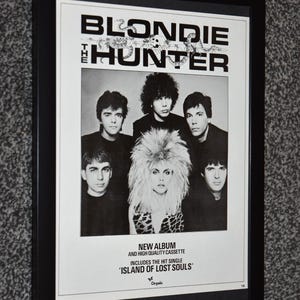May include: Black and white framed poster featuring the band Blondie. The poster includes the album title "The Hunter" and the text "New Album and High Quality Cassette" with the single "Island of Lost Souls". The band members are in the image.