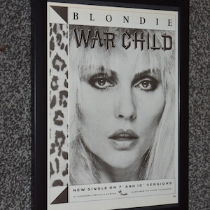 May include: Framed black and white Blondie "War Child" album art. The image features a close-up of a woman's face with the band's name and album title at the top. The text "New Single on 7" and 12" Versions" is at the bottom.
