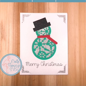 May include: A white card featuring a green snowman with a black hat and red scarf. The snowman has a white and silver glitter design. The card reads "Merry Christmas".