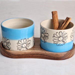 May include: A white ceramic mug with a black handle and the text "But First, Coffee" in a black, bold font. The mug is on a wooden surface. The mug is 10 cm tall.