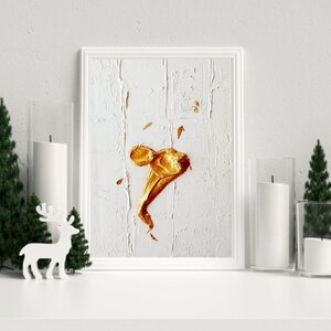 Puede incluir: Arte abstracto enmarcado en blanco con un fondo texturizado y un diseño central dorado. La obra de arte se exhibe sobre una superficie blanca, con velas y vegetación decorativa a ambos lados.