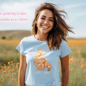 A smiling young woman in a wildflower farm field is wearing a light blue t-shirt printed with silkie chickens. Printed below the painted is the text Silkie Mama in a handwritten font. The text says that This painting is also available as a t-shirt.